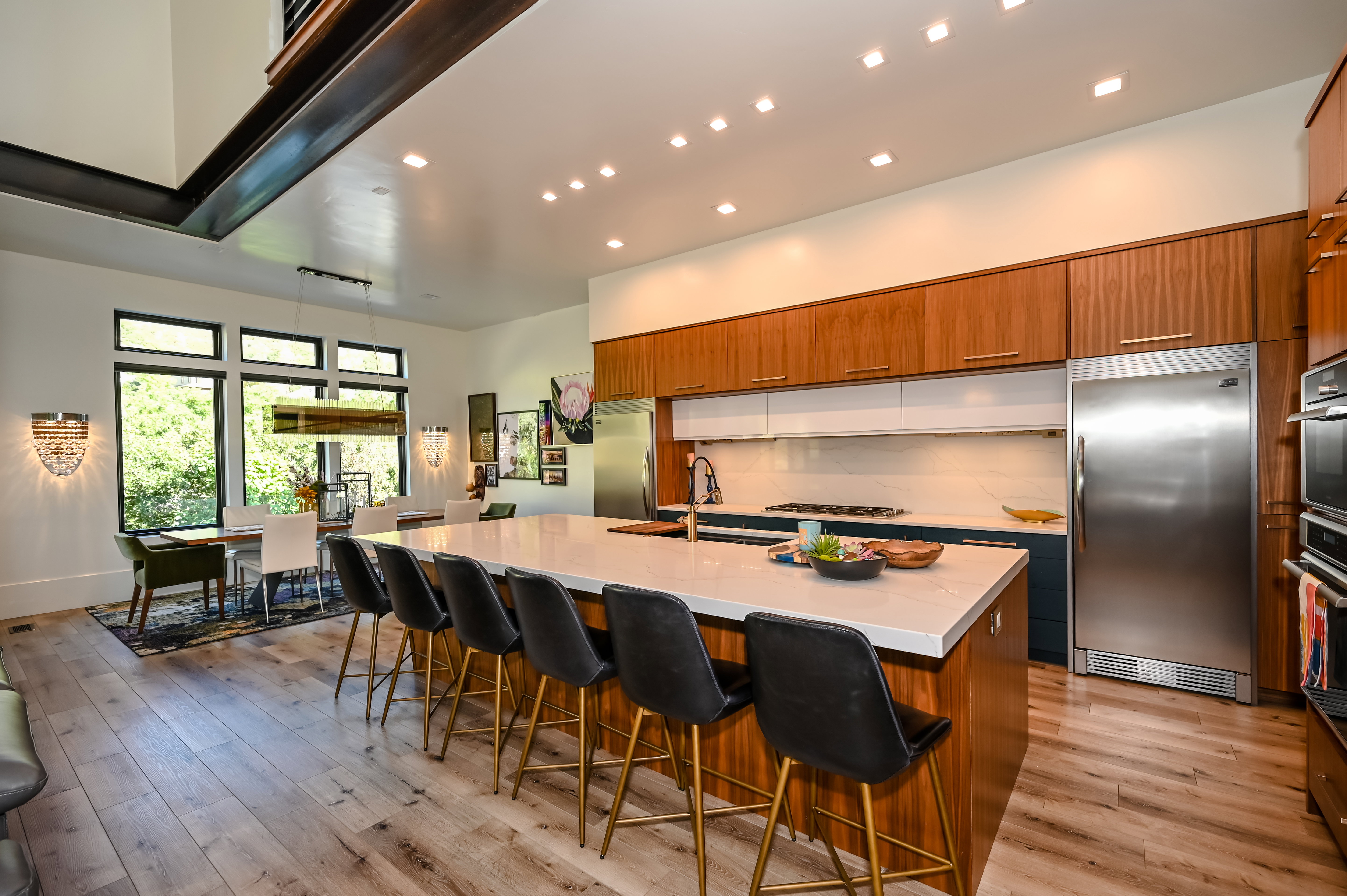 Modern kitchen featuring a large island with seating, stainless steel appliances, wood-finish flooring, and ample natural light from extensive windows