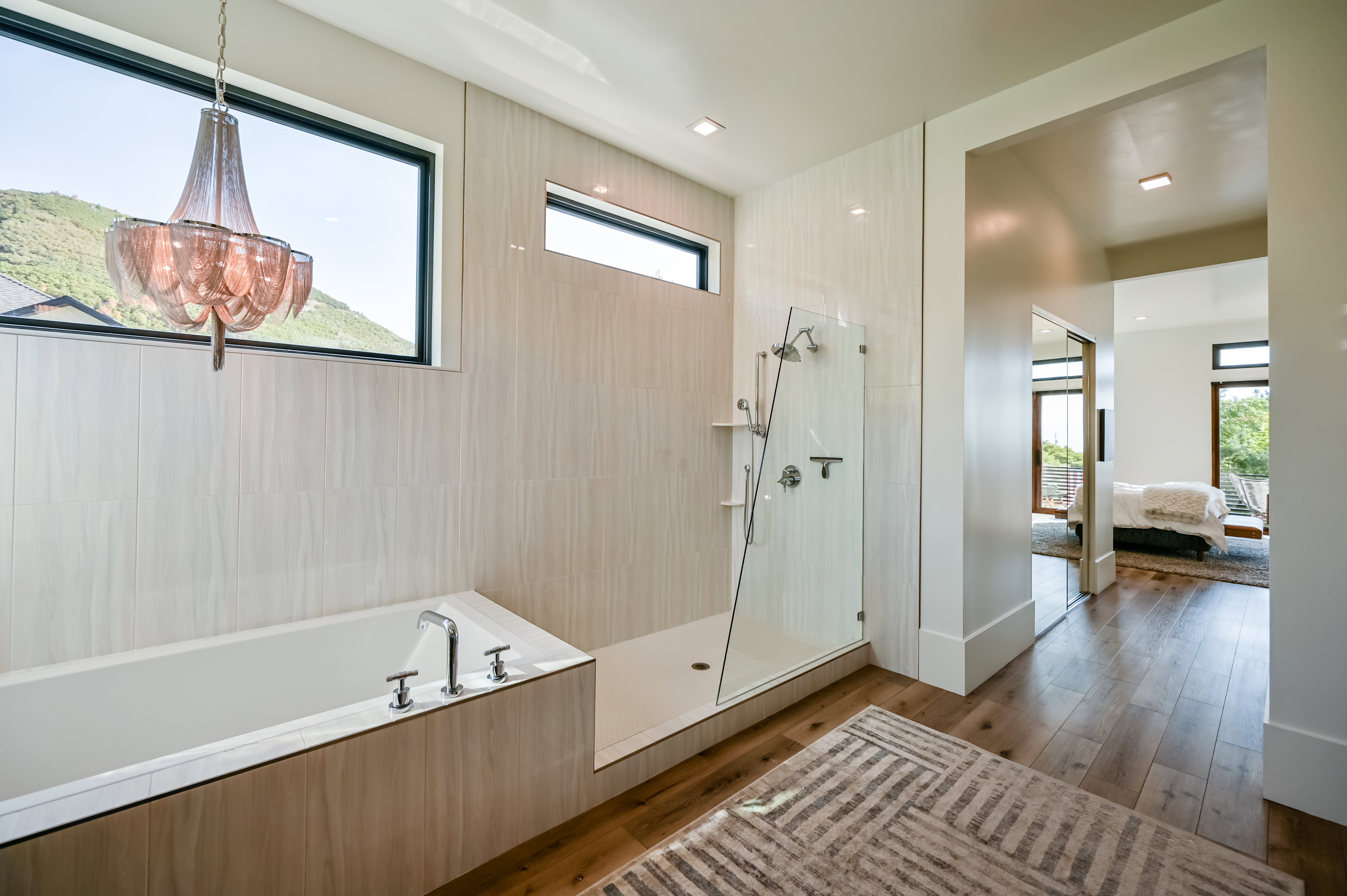 Freestanding soaking tub with chrome fixtures, glass-enclosed shower with multiple showerheads, and wood-finish flooring