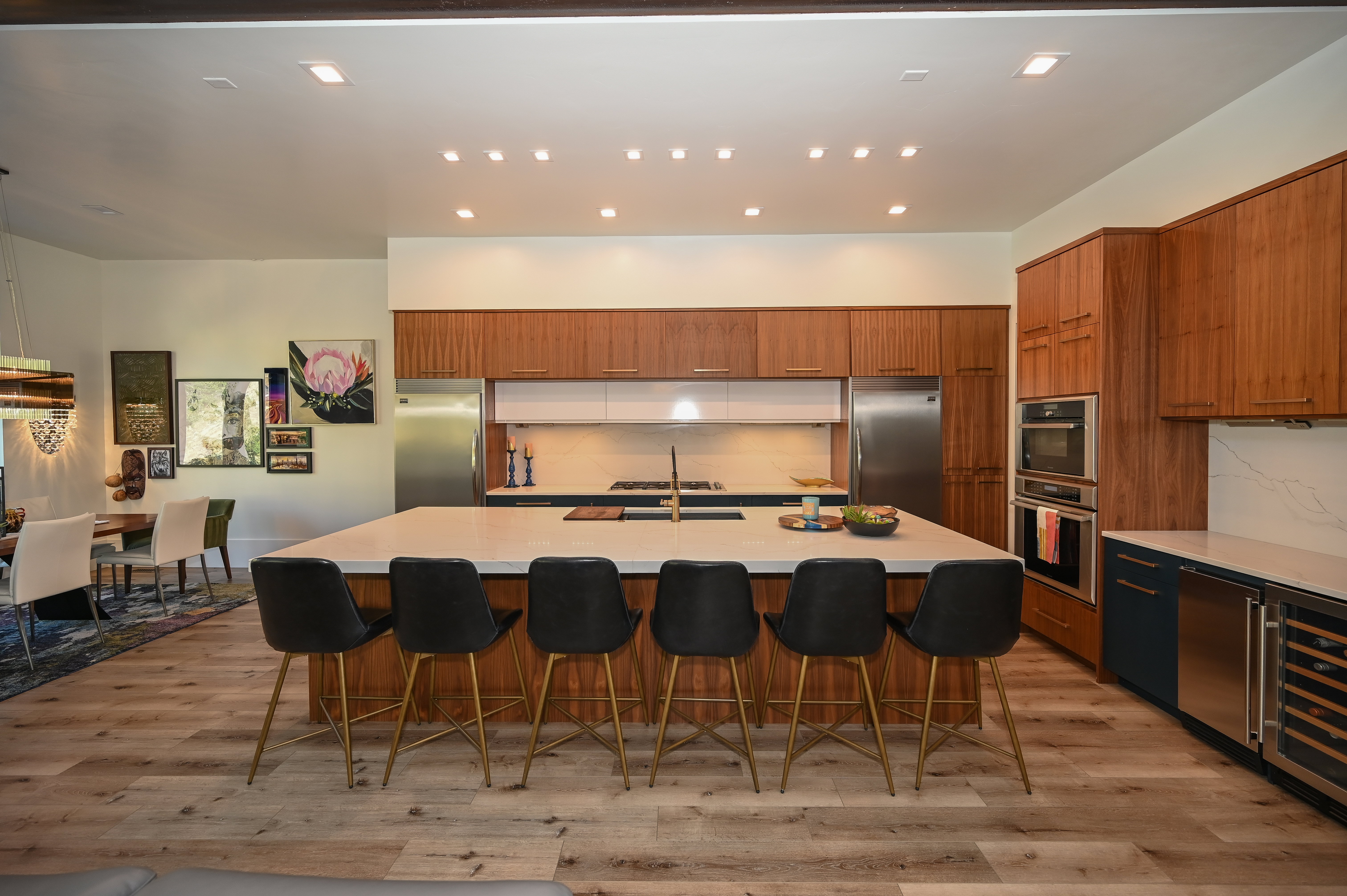 Expansive kitchen featuring a large central island with seating, wood-finish cabinetry, integrated stainless steel appliances, and wood-finish flooring