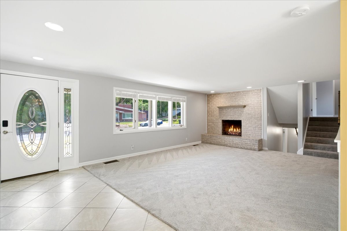 Spacious living area featuring a brick-surround fireplace, light gray wall paint, recessed lighting, and a front entry door with leaded glass