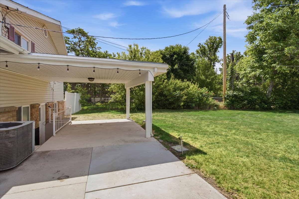 Covered concrete patio with string lighting and a ceiling-mounted fixture. Grass has been digitally enhanced. Grass is not fully green in all areas.