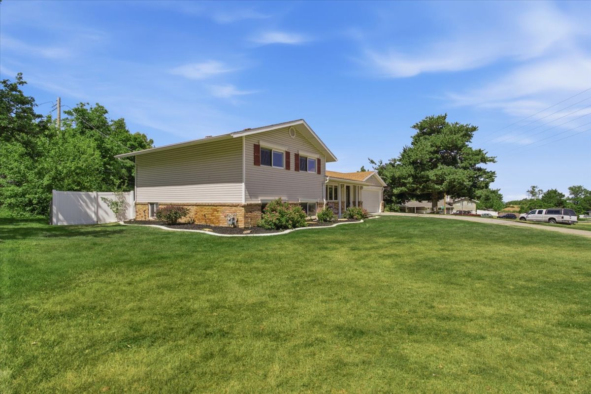 Split-level residence featuring light-colored siding and a stone facade. Grass has been digitally enhanced. Grass is not fully green in all areas.