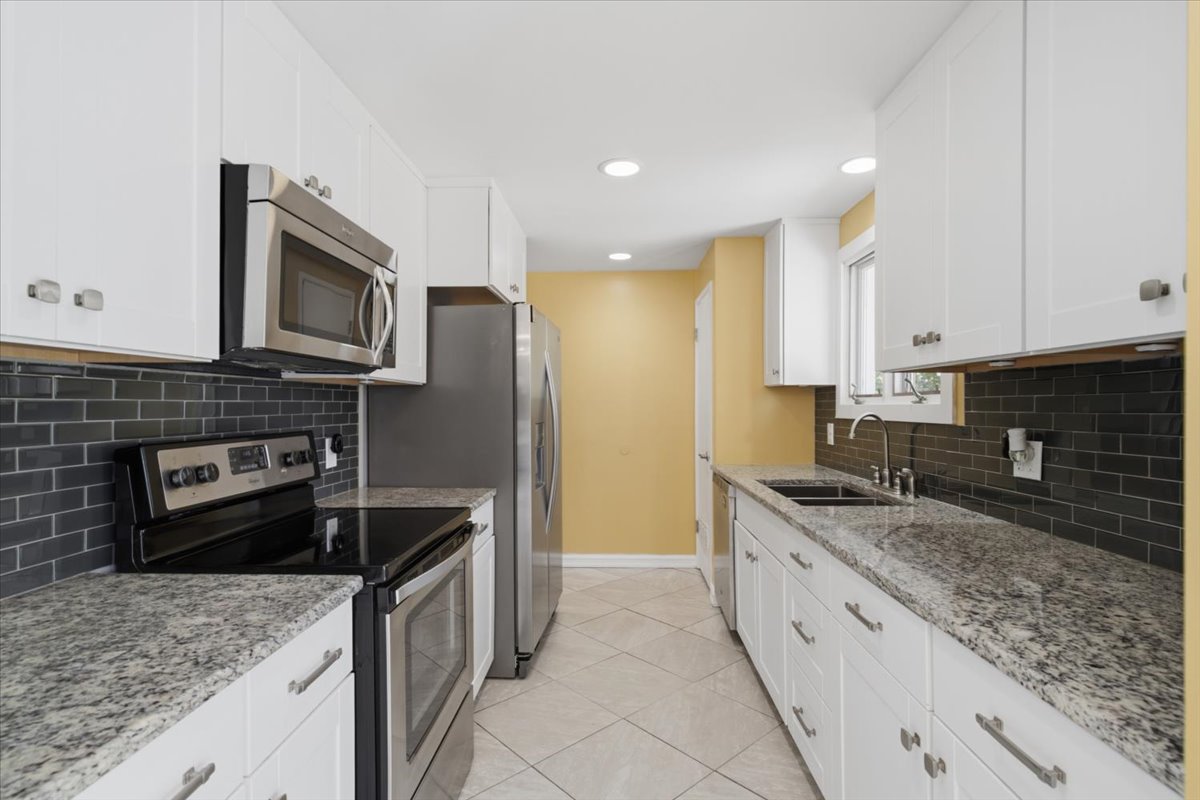 Galley kitchen featuring white cabinetry, granite countertops, stainless steel appliances, a dark subway tile backsplash, and recessed lighting