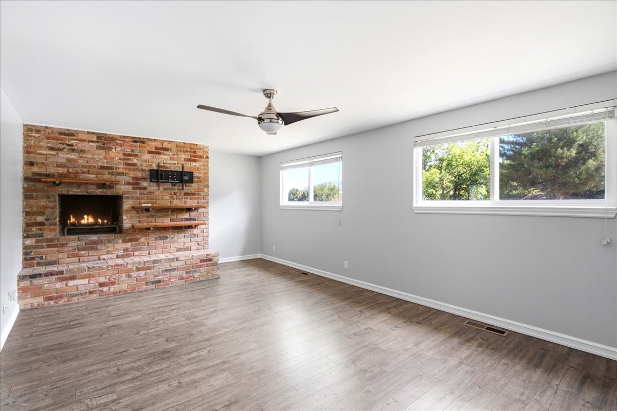 Living area featuring a brick fireplace with a built-in firebox, floating wood shelves, and wood-finish flooring