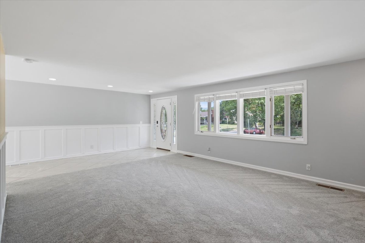 Spacious living area featuring new gray carpet, wainscoting, recessed lighting, and a decorative front entry door with a frosted oval glass insert