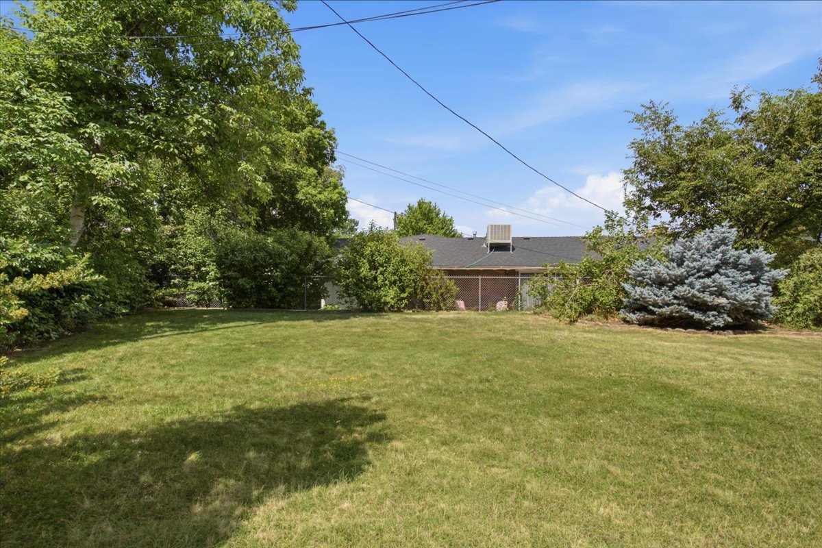 Spacious backyard featuring a lush lawn, mature trees, and established shrubbery providing perimeter privacy. Grass has been digitally enhanced. Grass is not fully green in all areas.