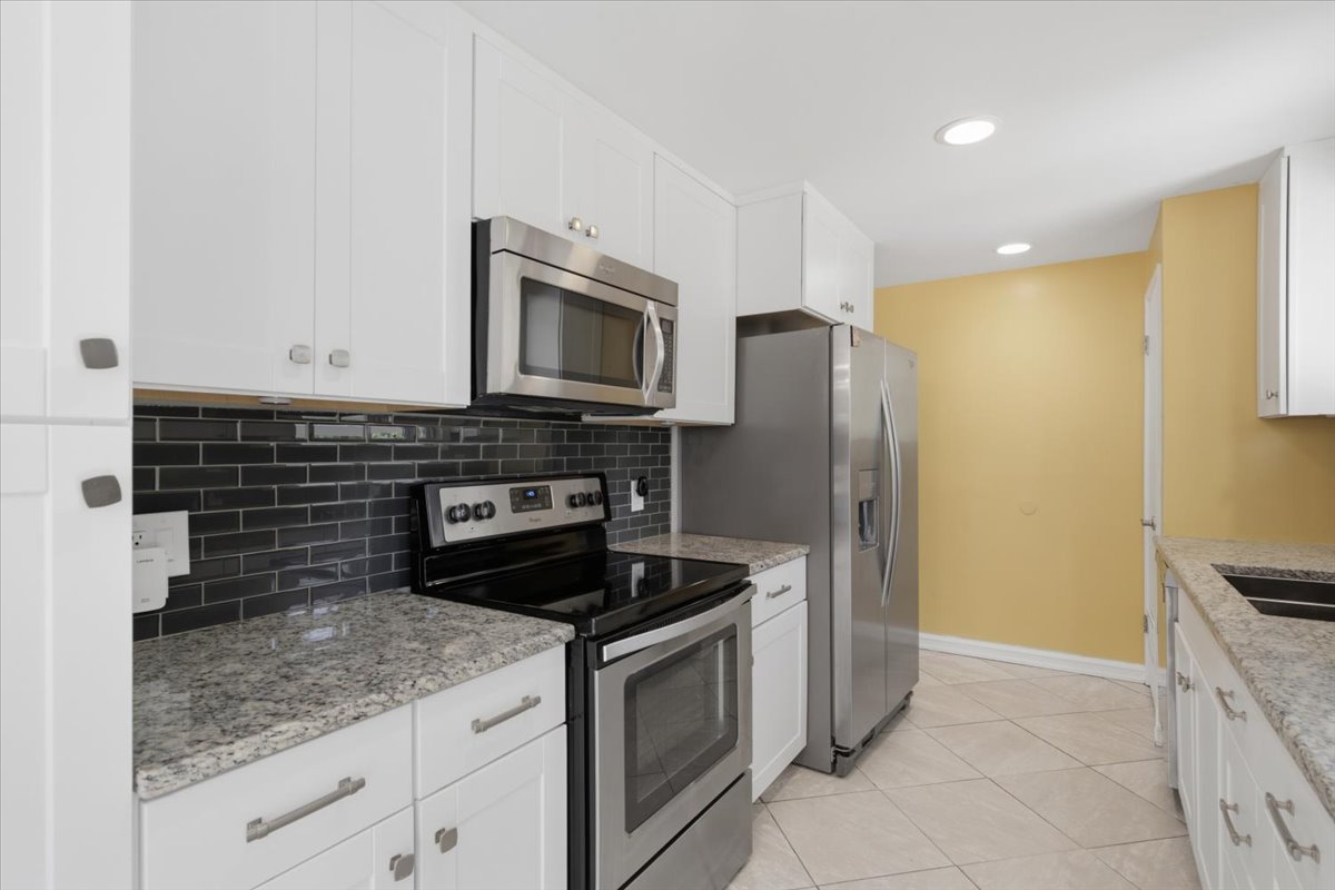 Modern kitchen featuring white cabinetry, granite countertops, stainless steel appliances, a dark subway tile backsplash, and recessed lighting