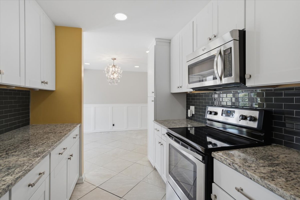 Kitchen featuring white shaker-style cabinetry, granite countertops, and dark subway tile backsplash
