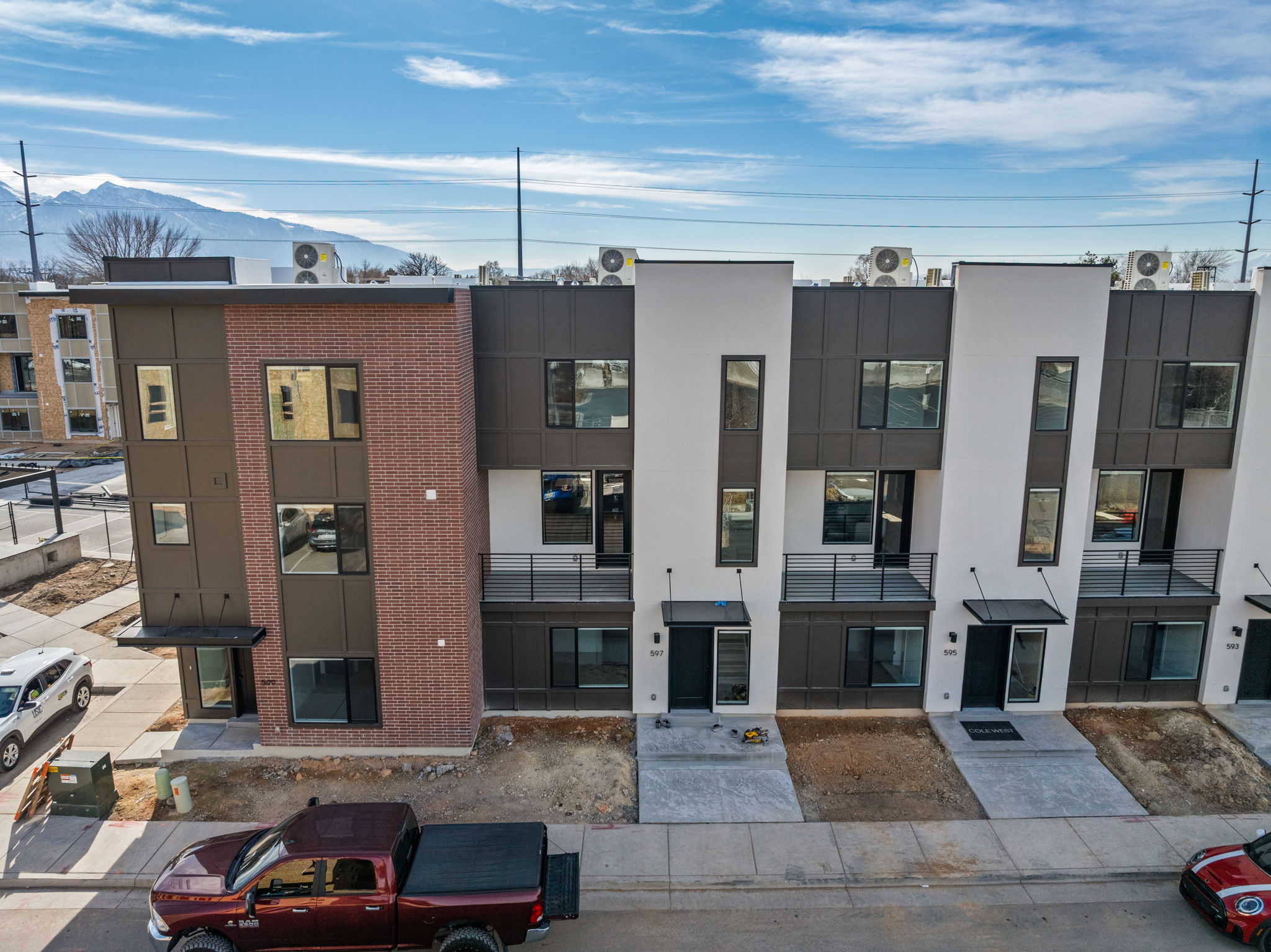 Contemporary townhomes featuring a multi-textured facade with brick, dark paneling, and white stucco