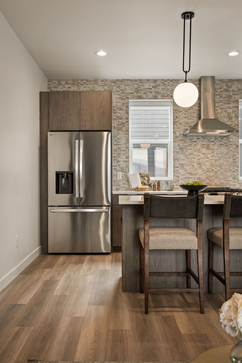 Modern kitchen space featuring stainless steel appliances, wood-finish flooring, recessed lighting, and a textured stone backsplash
