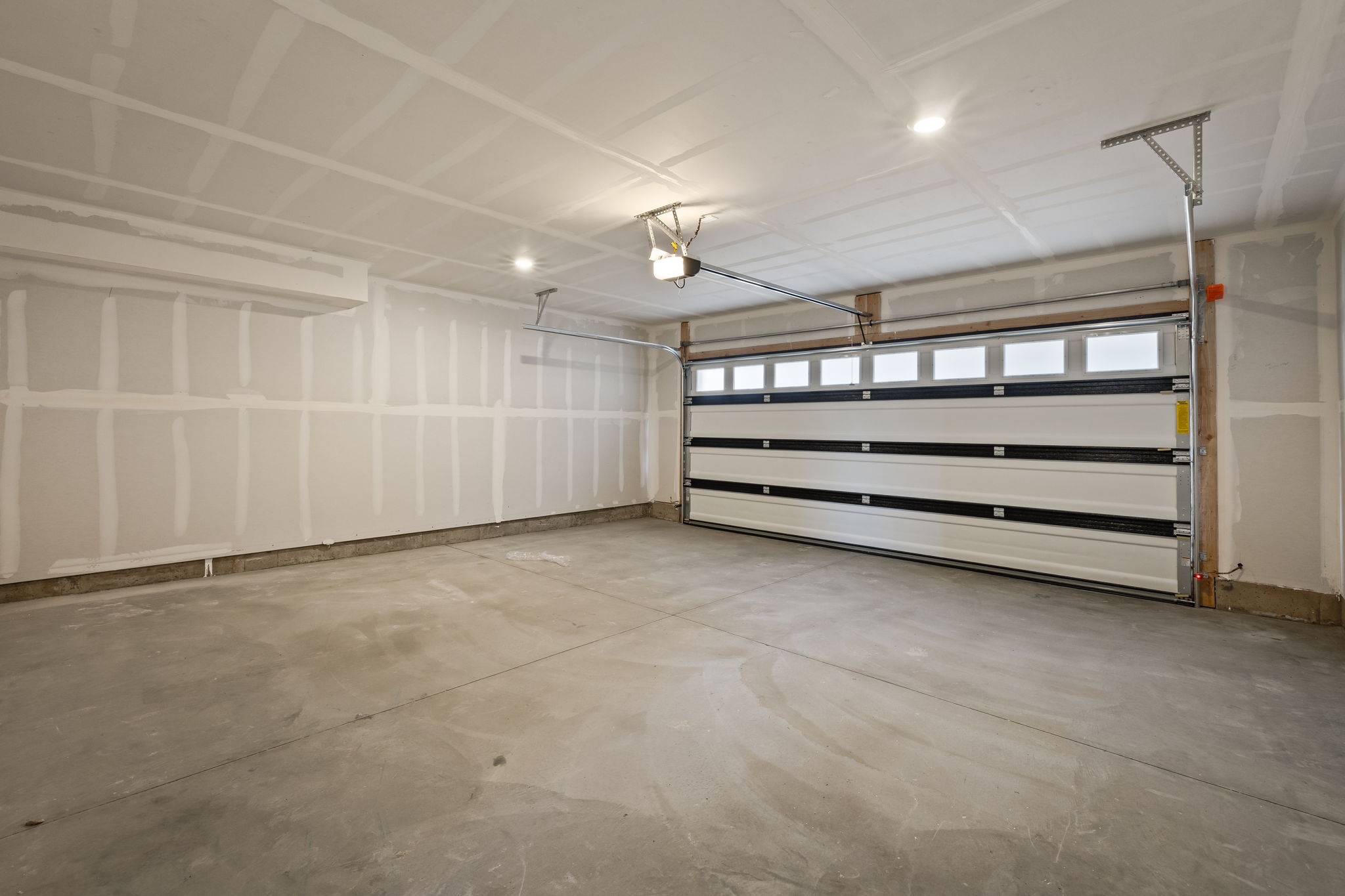 Spacious garage featuring a concrete floor, bright overhead lighting, and a white paneled garage door with upper windows