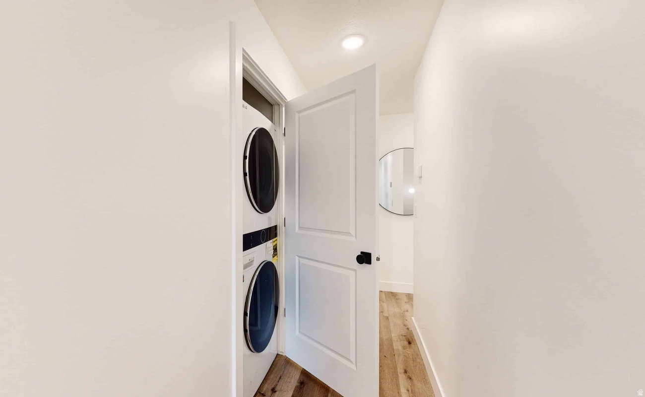 Integrated laundry closet featuring a stacked washer and dryer, white paneled door with black hardware, and recessed lighting