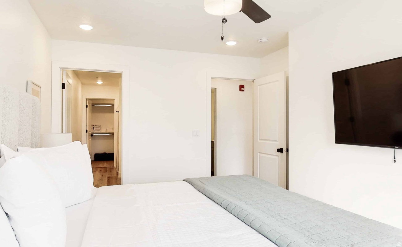 Well-lit interior featuring a ceiling fan with integrated lighting, recessed overhead lighting, a wall-mounted flat-screen television, and white paneled doors with black hardware