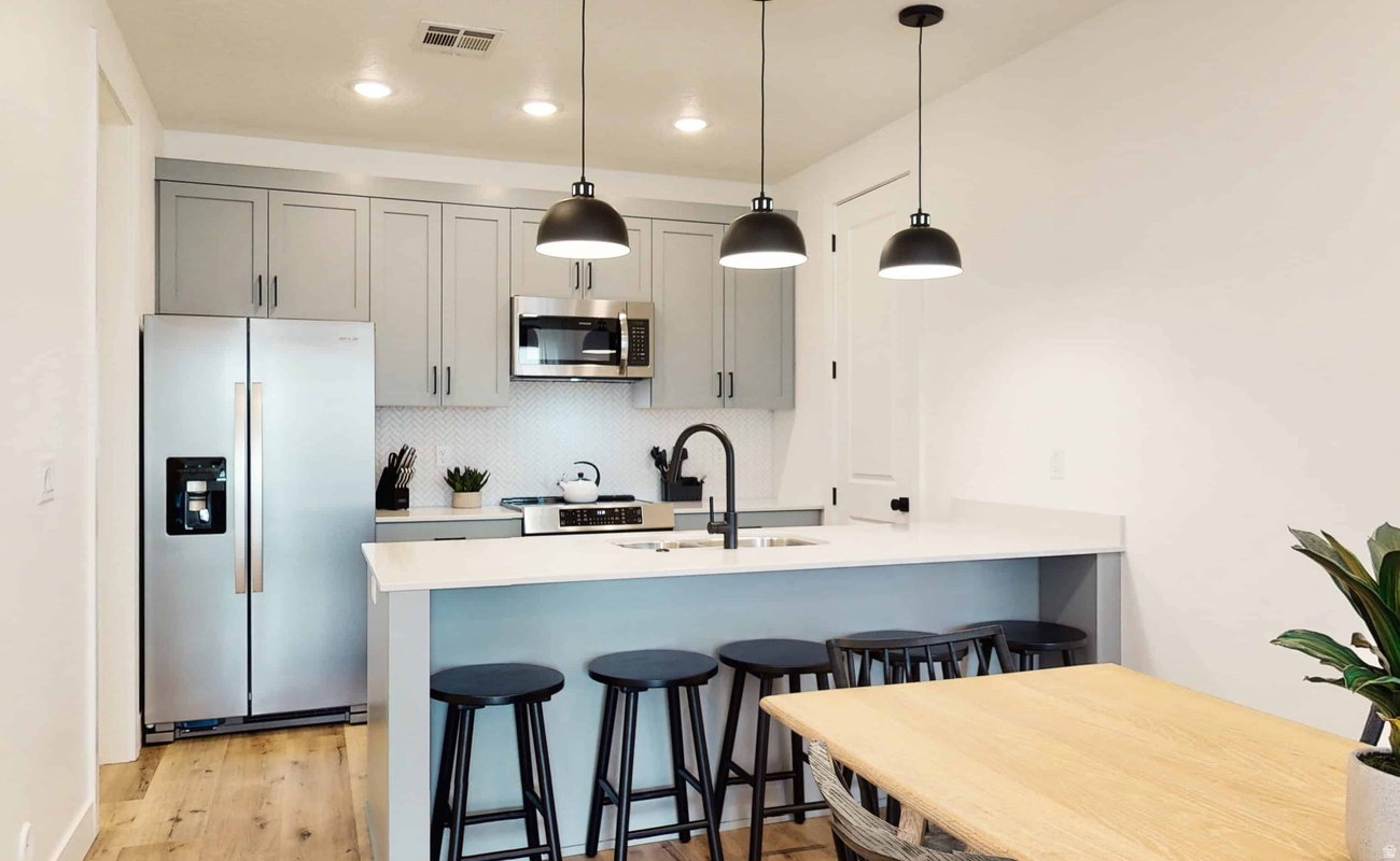Modern kitchen featuring light gray cabinetry, stainless steel appliances, white hexagon tile backsplash, and an island with pendant lighting