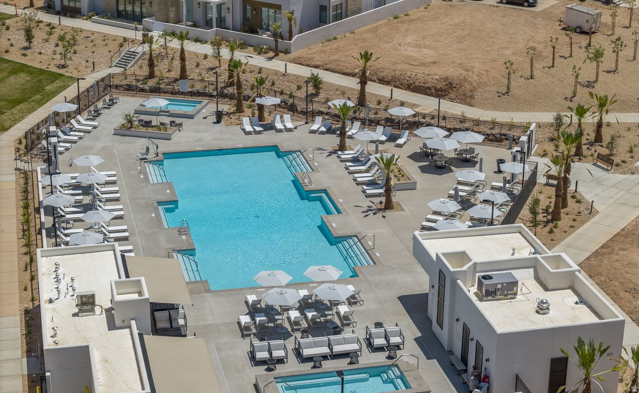 Community pool area featuring a large swimming pool with integrated steps, multiple lounge areas, a separate spa, and surrounding hardscaping