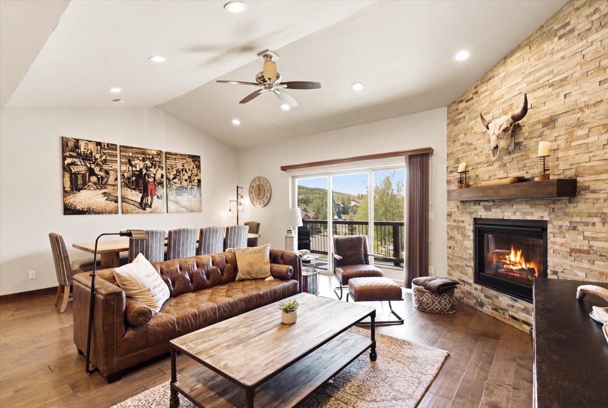 Spacious living area featuring a stacked stone fireplace with wood mantle, vaulted ceilings, recessed lighting, and wood-finish flooring
