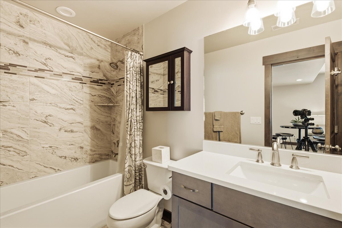 Bathroom featuring a deep bathtub, a tiled shower surround with a decorative accent band, a built-in shower shelf, a vanity with a white countertop, and a mirrored medicine cabinet