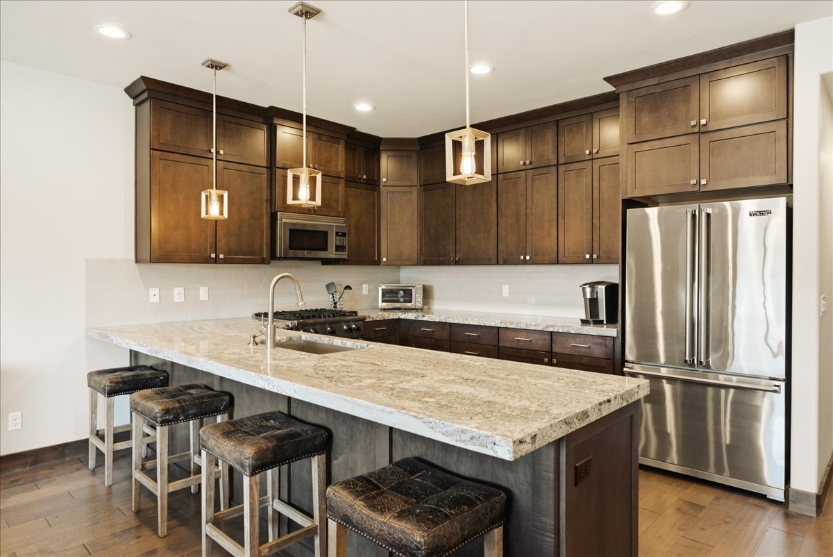 Spacious kitchen featuring dark wood cabinetry, a large kitchen island with a light-toned countertop, stainless steel appliances, and wood-finish flooring