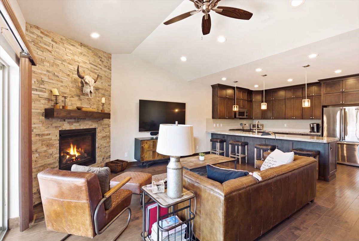 Open-concept living space featuring wood-finish flooring, a stone-clad fireplace with a wood mantle, and recessed lighting