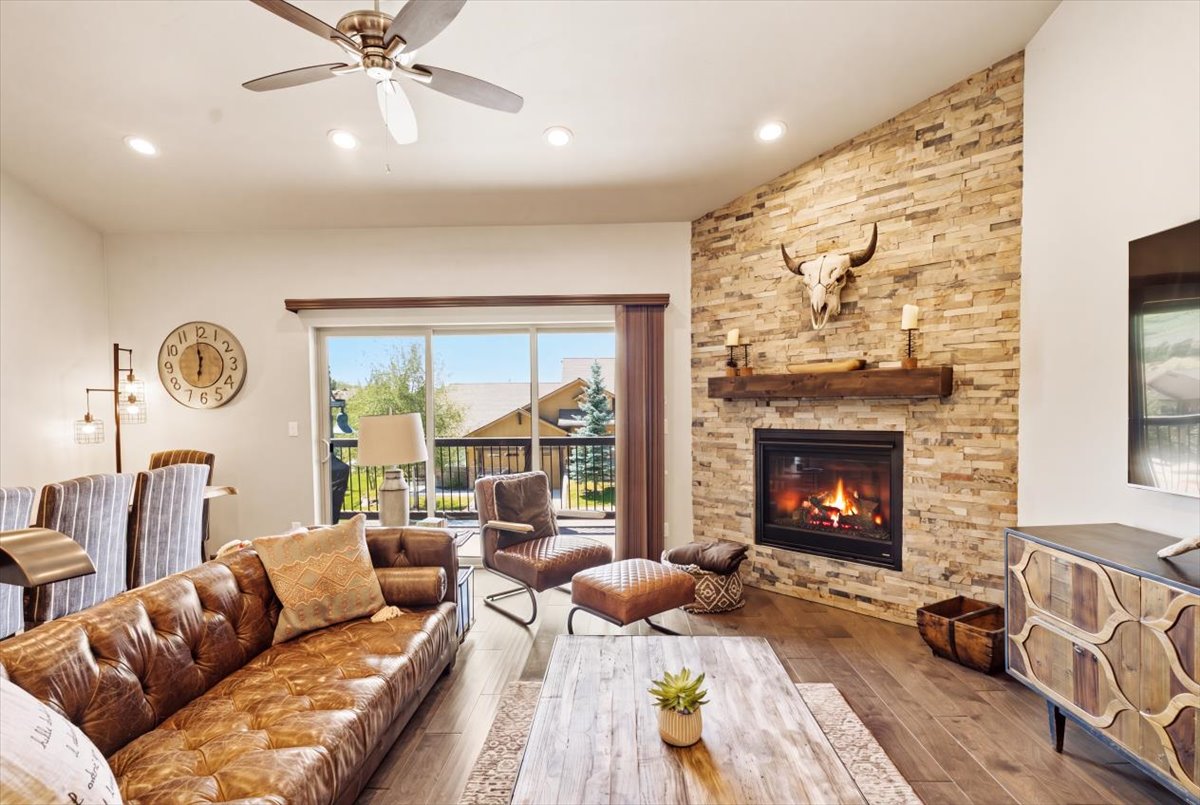 Living area featuring a stone veneer fireplace with a rustic wood mantel, large sliding glass doors, recessed lighting, and a ceiling fan