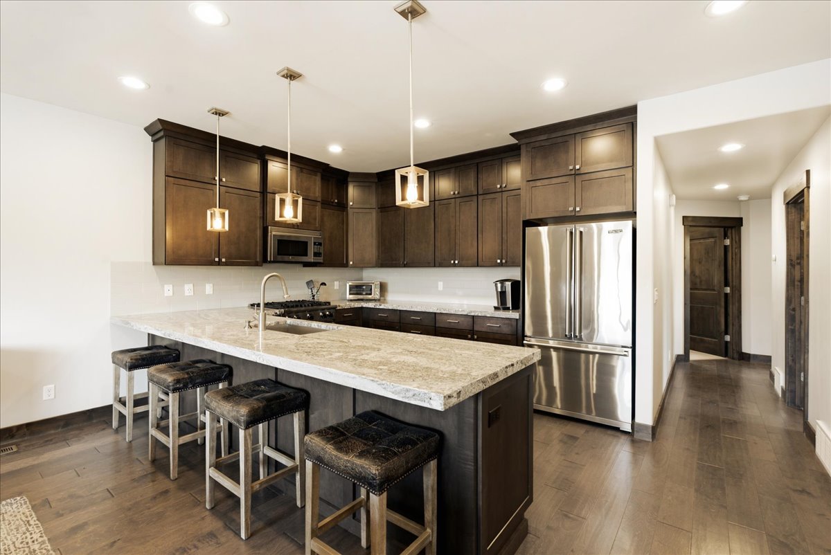 Kitchen featuring dark wood cabinetry, stainless steel appliances, a light-toned countertop island with sink, and recessed lighting