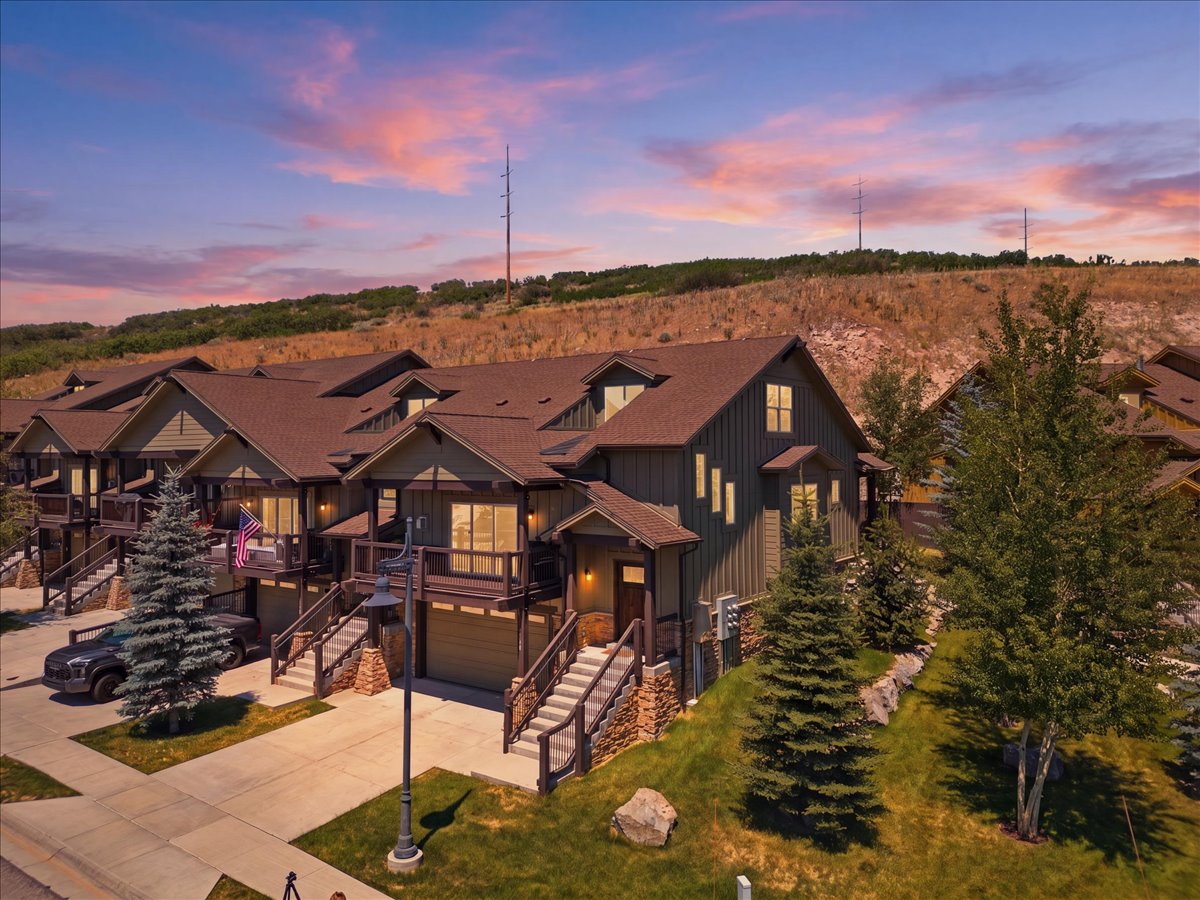 Townhome featuring a brown roof, dark green siding, and stone accents