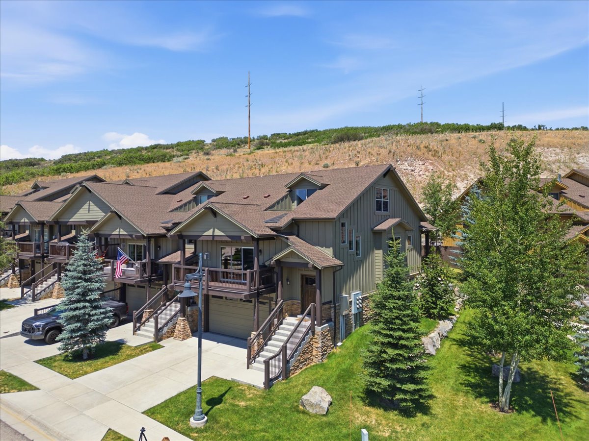 Townhome exterior featuring board and batten siding, stone accents, a covered front porch, an attached garage, and a private balcony