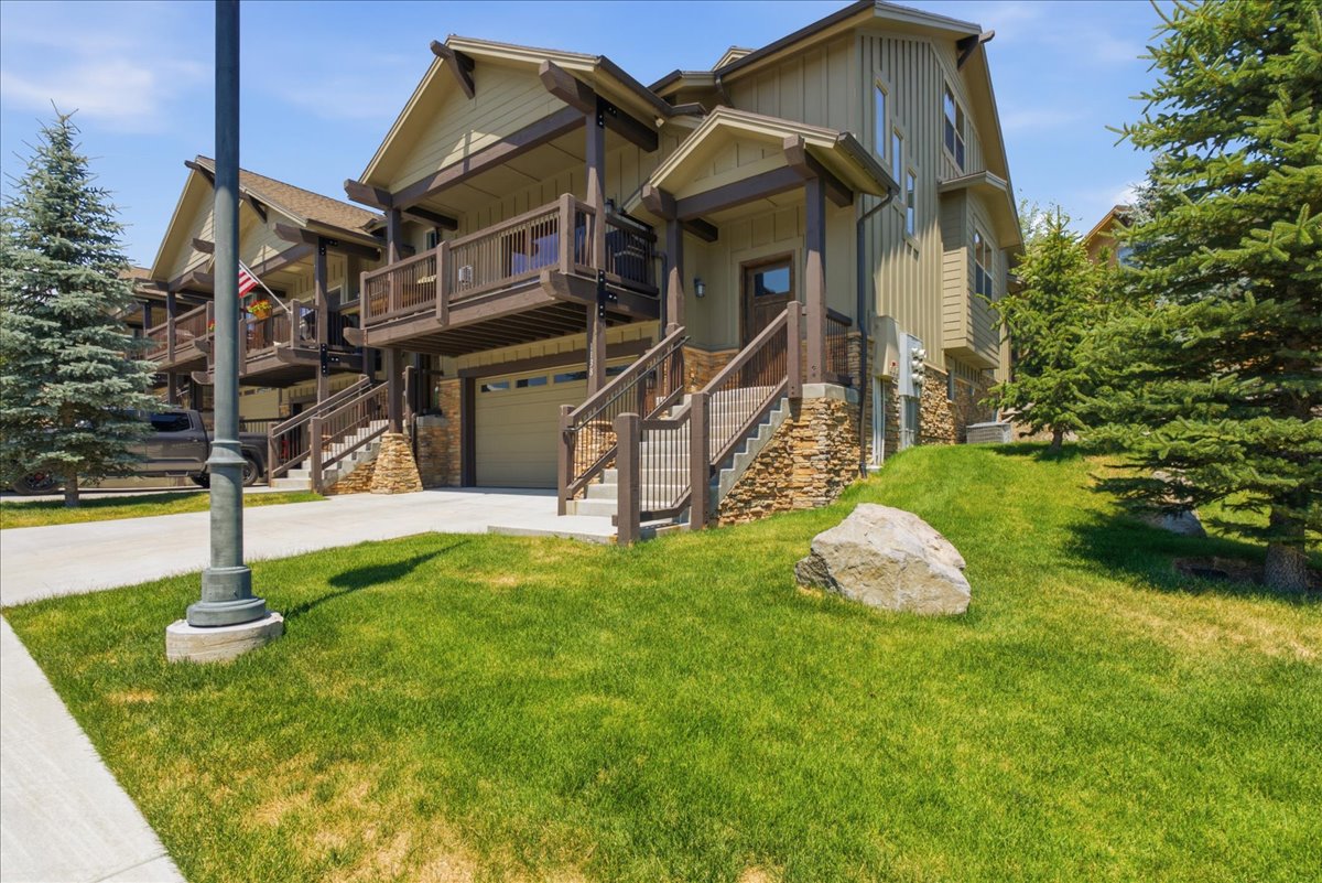 Craftsman-style townhome exterior featuring stone accents, wood-finish siding, balcony, a ground-level garage, and mature evergreen landscaping