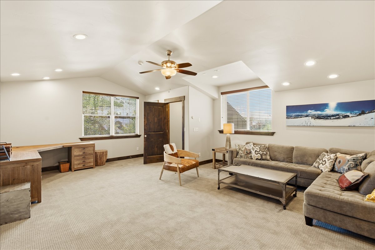 Vaulted ceiling top floor room featuring recessed lighting, a ceiling fan, two windows with wood trim, and a dark wood-finish door