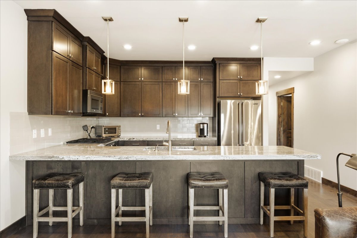 Kitchen featuring dark wood cabinetry, a large center island with seating, stainless steel appliances, a tile backsplash, and recessed lighting