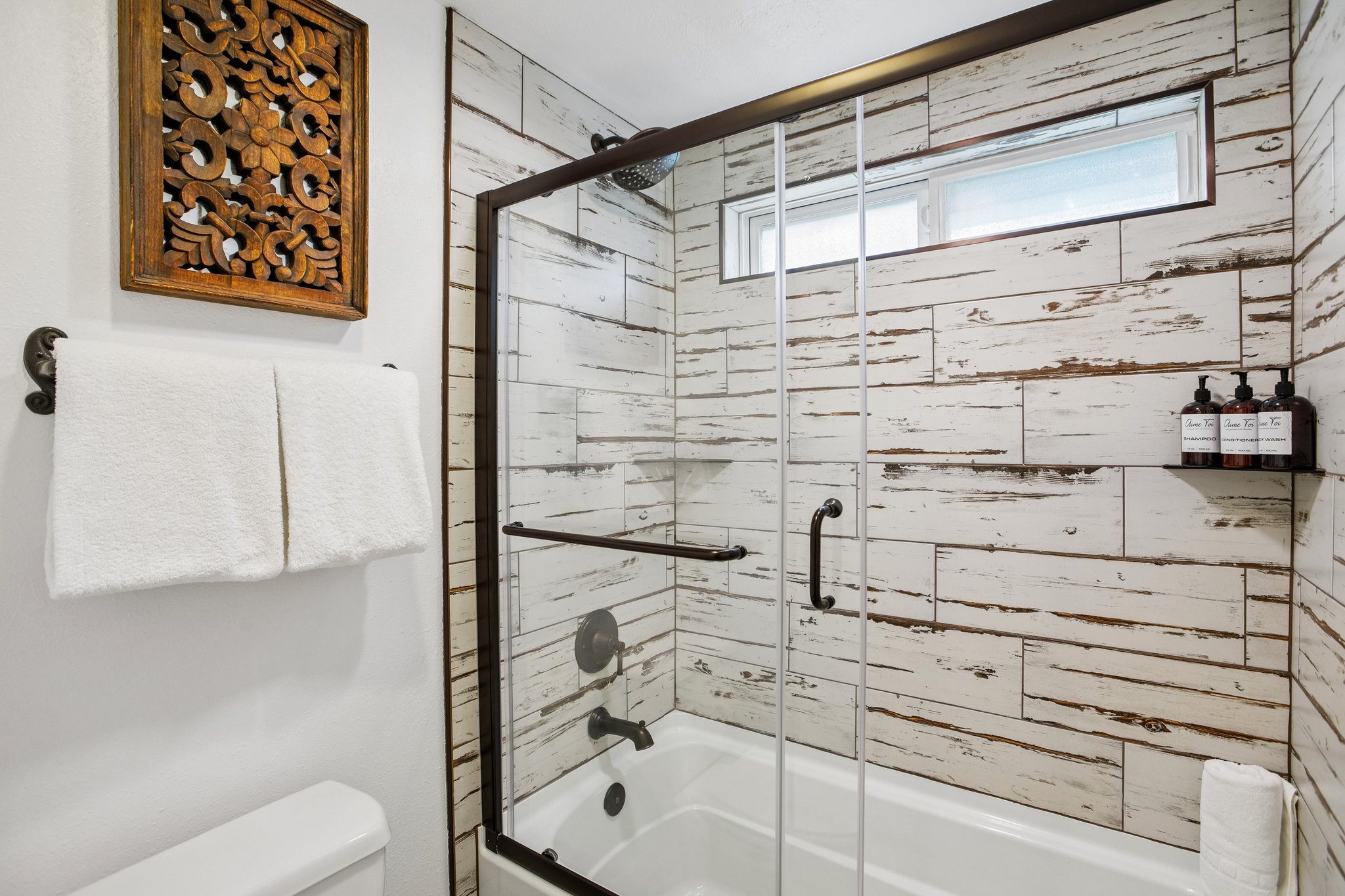 Bathroom shower-tub combination featuring a glass enclosure with dark bronze framing, distressed wood-finish tile surround, and a horizontal window