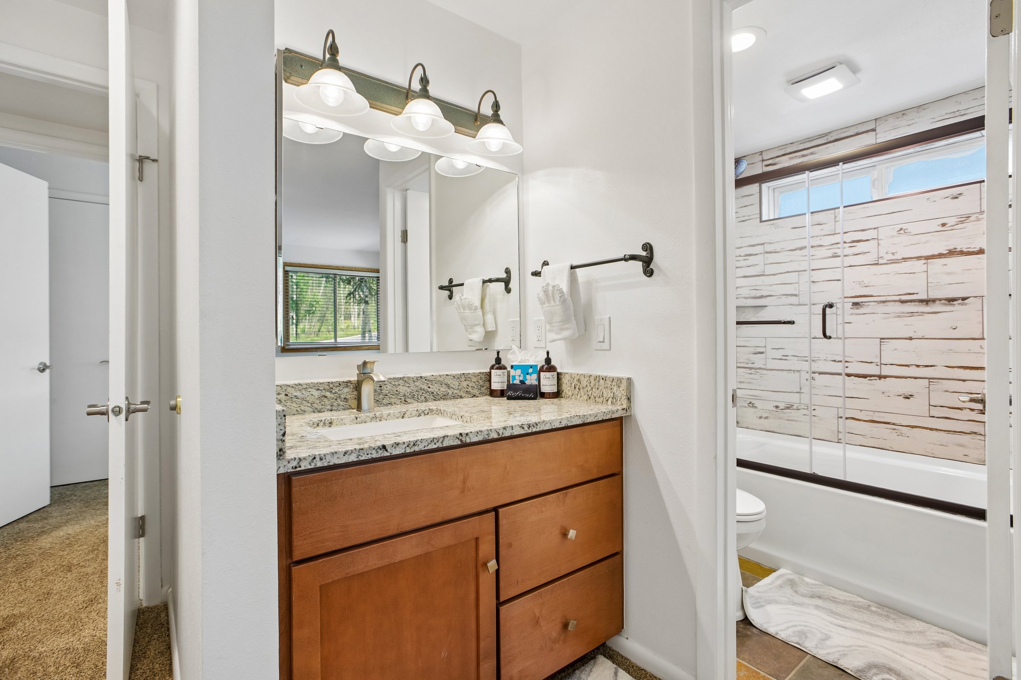 Bathroom featuring a wood vanity with a granite-style countertop, undermount sink, and a framed mirror