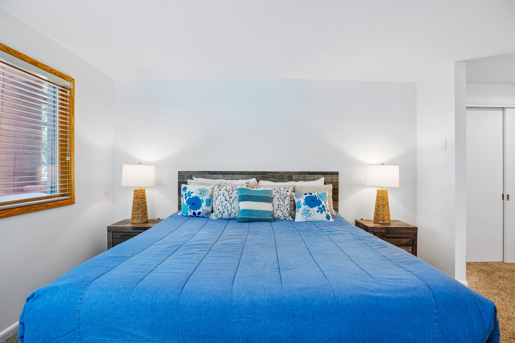 Spacious room featuring a wood-frame window with horizontal blinds, neutral wall finishes, and carpet flooring
