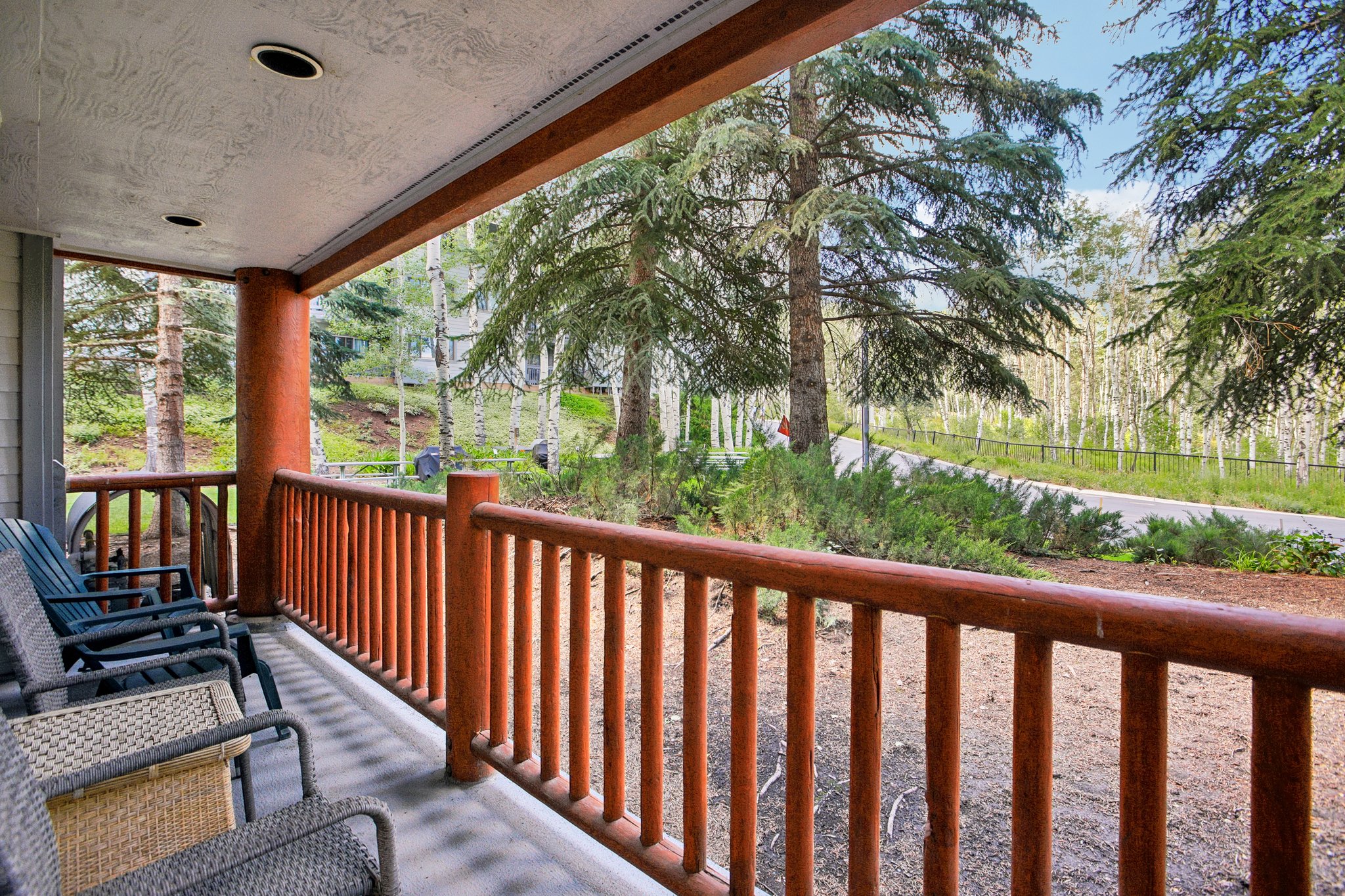 Covered patio featuring log-style railings and columns, recessed lighting, and a natural tree-lined backdrop