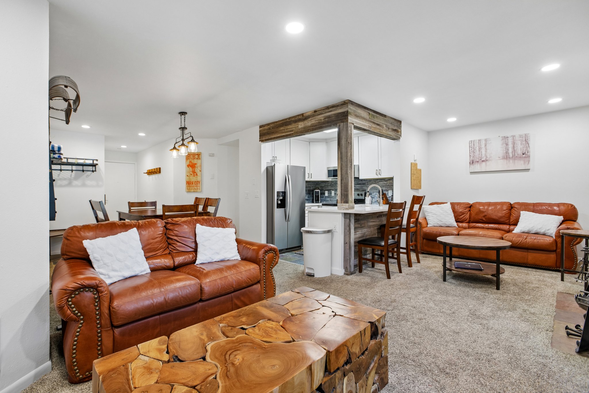 Open-concept living space featuring recessed lighting, carpeted flooring, and a kitchen bar with wood-finish paneling and seating