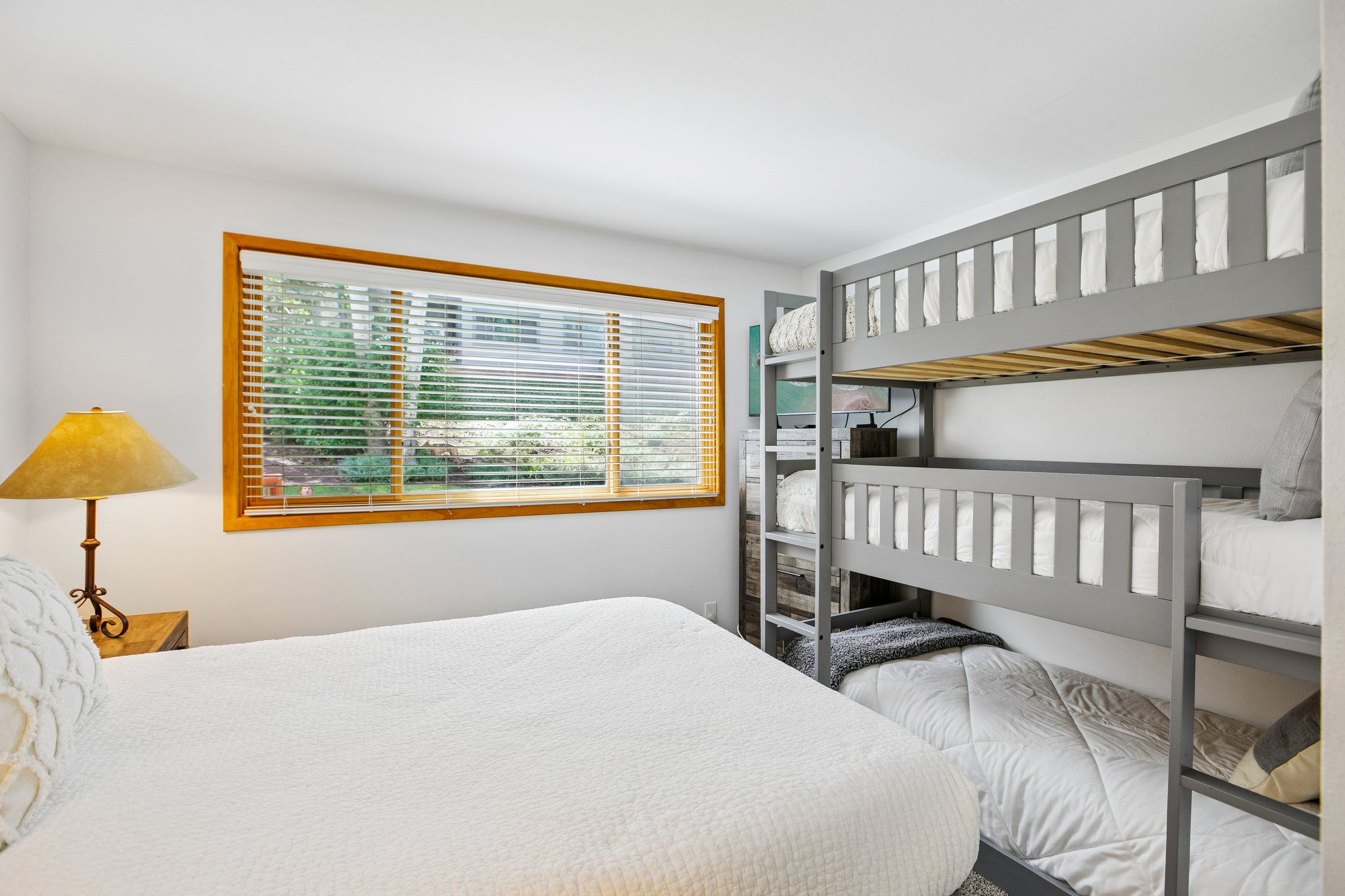 Bright sleeping area featuring a triple bunk bed, a window with wood framing, and white walls