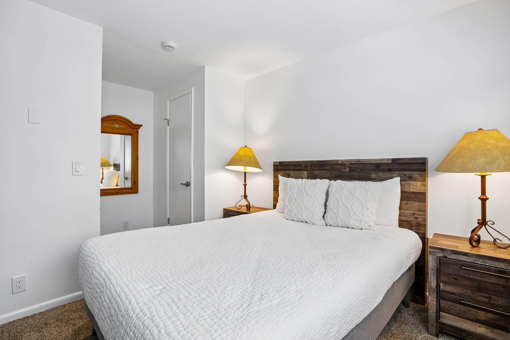 Bedroom featuring a wood-finish headboard, wood-finish nightstands, wall-to-wall carpeting, and bright white walls