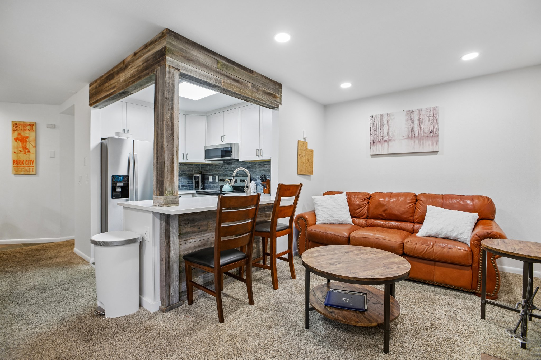 Open-concept living space featuring a breakfast bar with seating, wood-finish accents, white cabinetry, stainless steel appliances, and recessed lighting