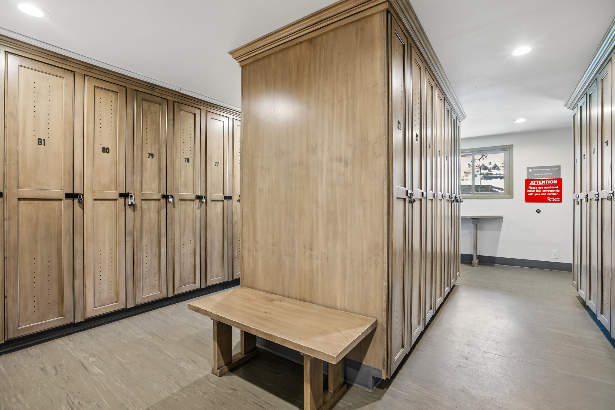 Locker room featuring extensive wood-finish lockers with black hardware, recessed lighting, and wood-finish flooring