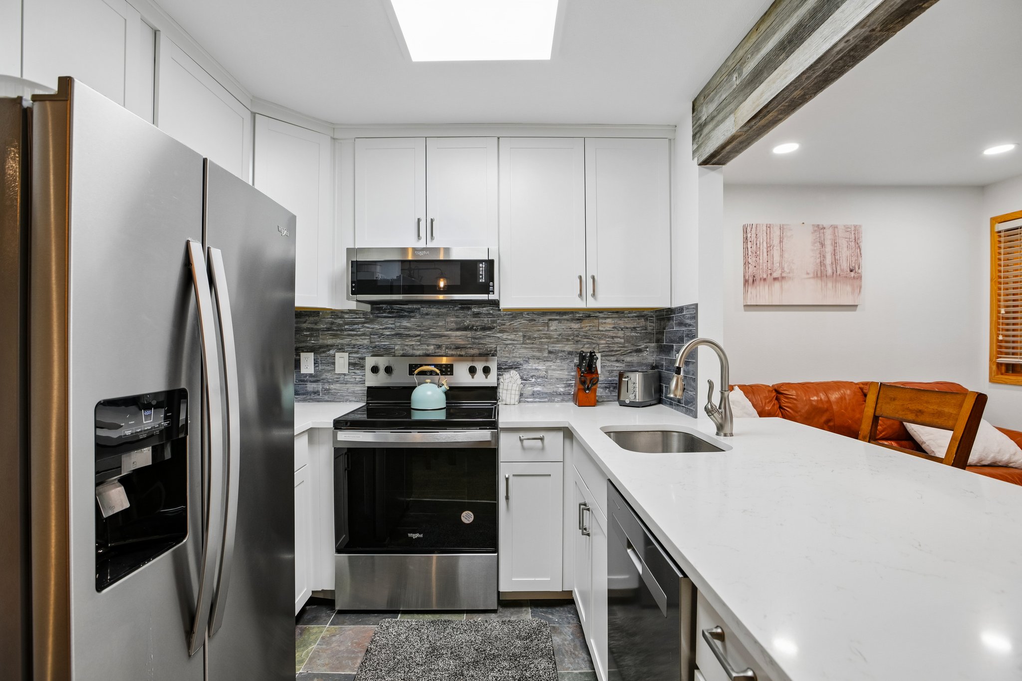 Modern kitchen featuring stainless steel appliances, white cabinetry, a skylight, a quartz countertop, and a tile backsplash