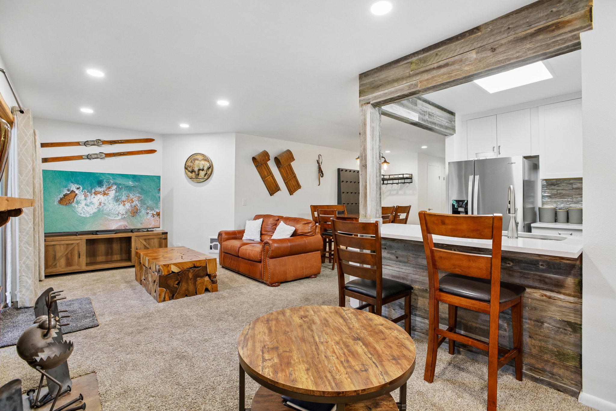 Open-concept living space featuring recessed lighting, a kitchen pass-through with a breakfast bar, white cabinetry, a stainless steel refrigerator, and wood-finish accents