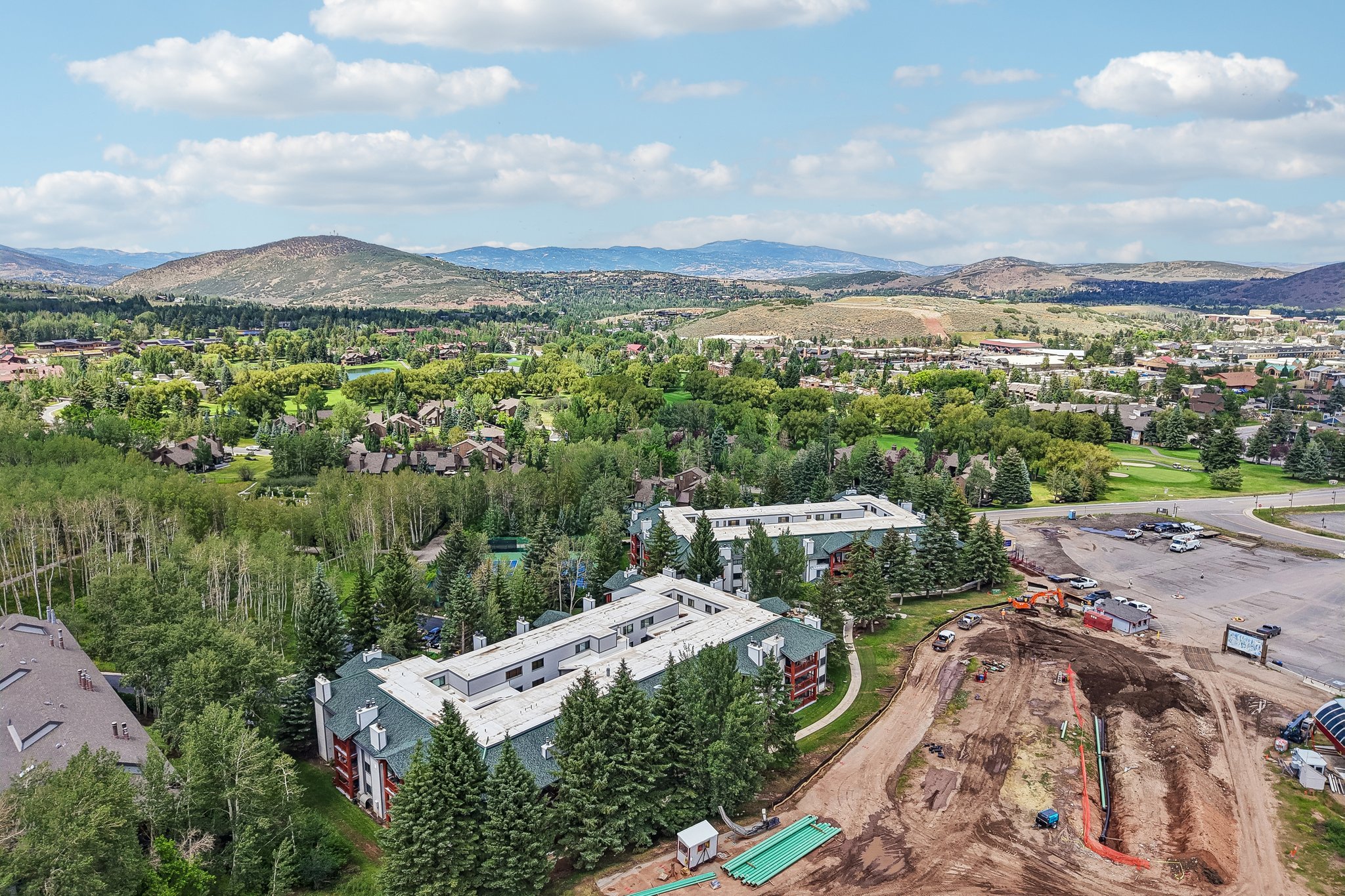 Expansive aerial showcasing a complex of buildings with green sloped roofs amidst dense mature trees