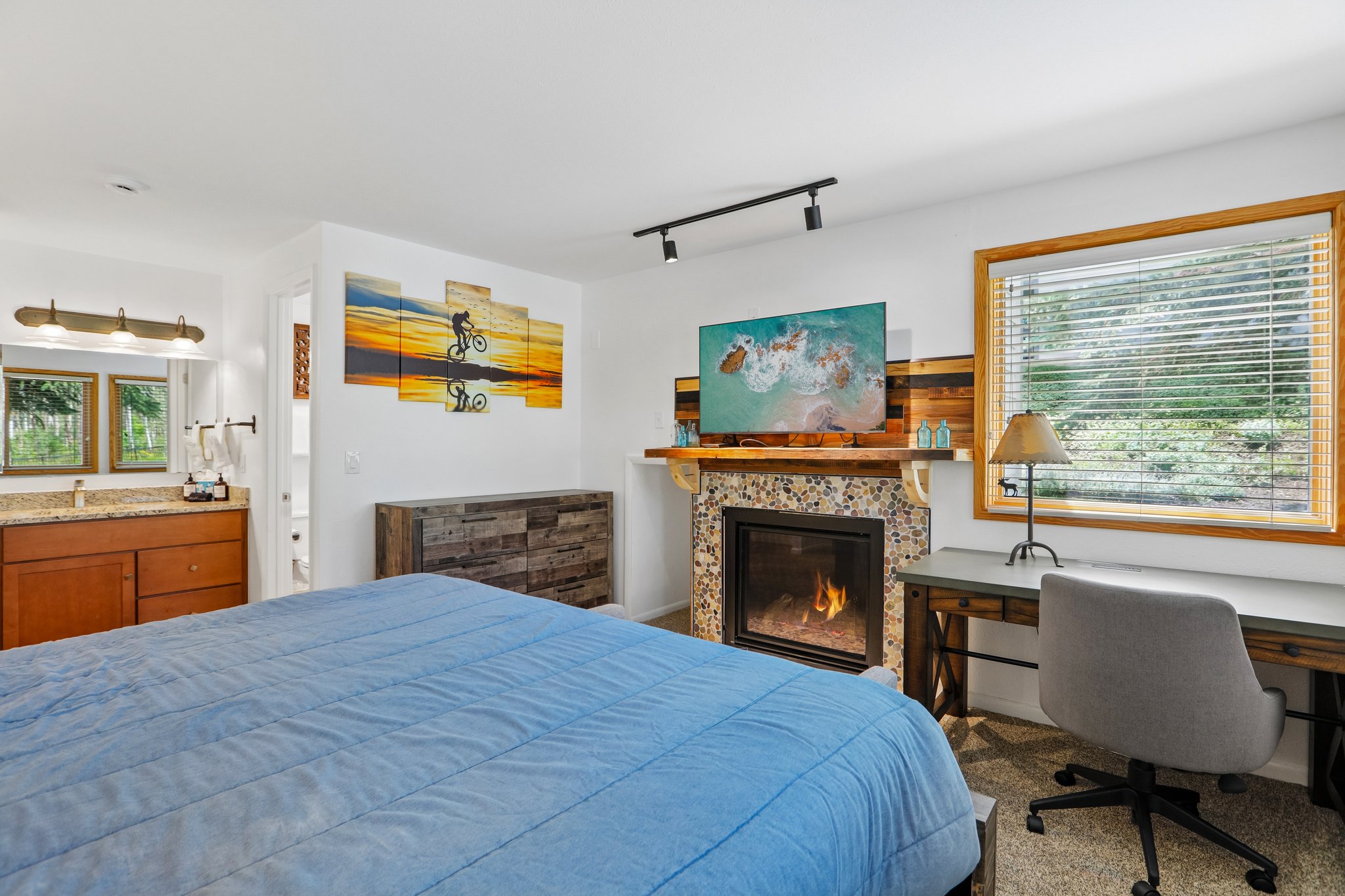 Bedroom featuring a stone-surround fireplace with a wood mantel, a window with wood trim, and a built-in vanity with a stone countertop