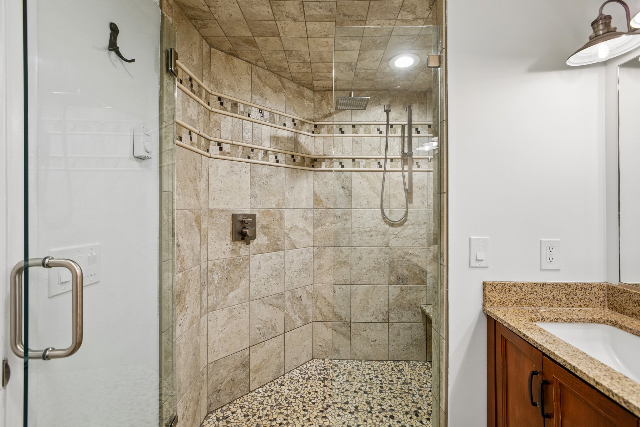 Glass-enclosed shower featuring natural stone-look wall tiling with an accent band, a built-in bench, pebble floor, and a rain showerhead
