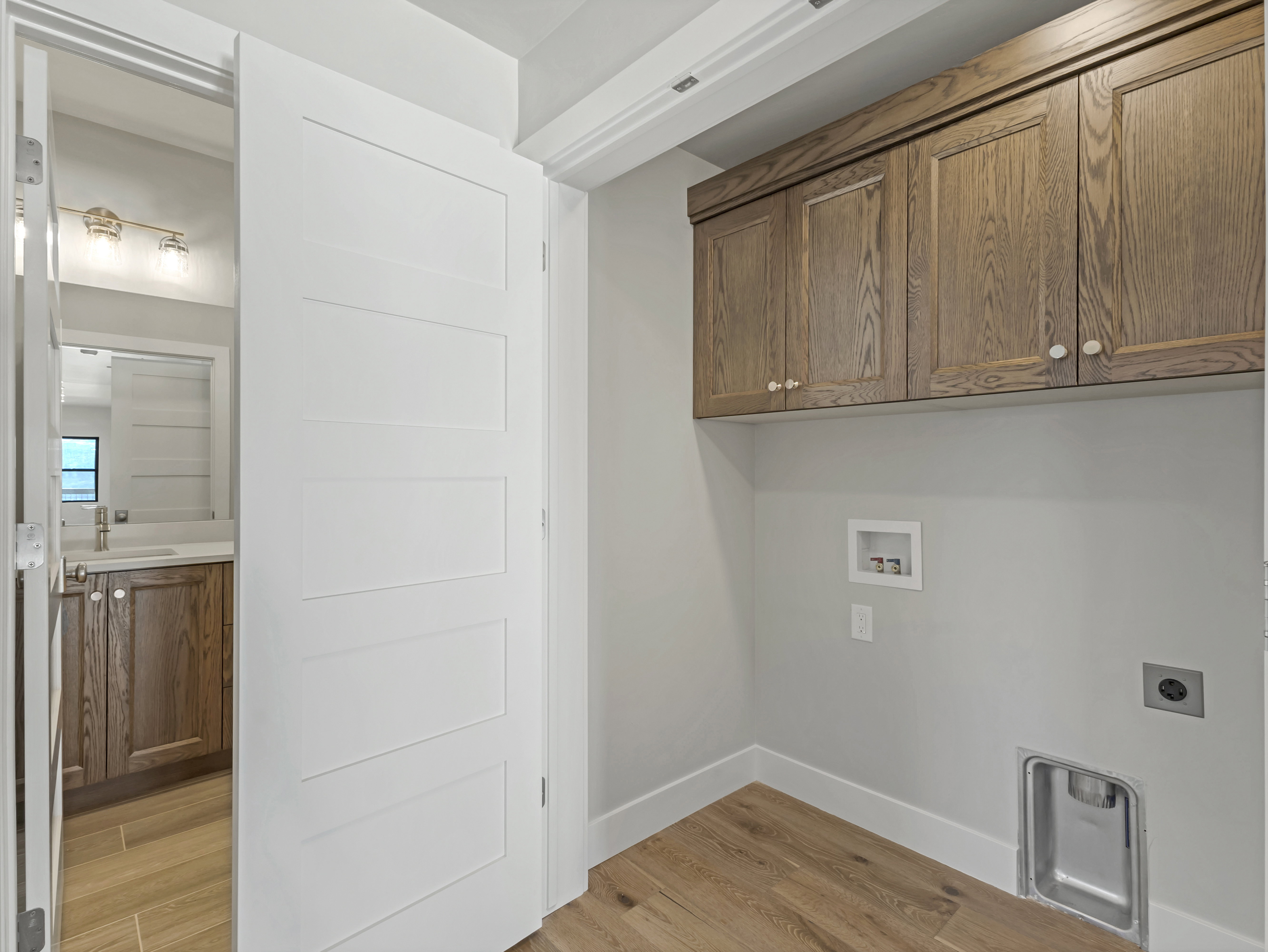 Dedicated laundry area featuring wood-finish flooring and upper wood cabinetry