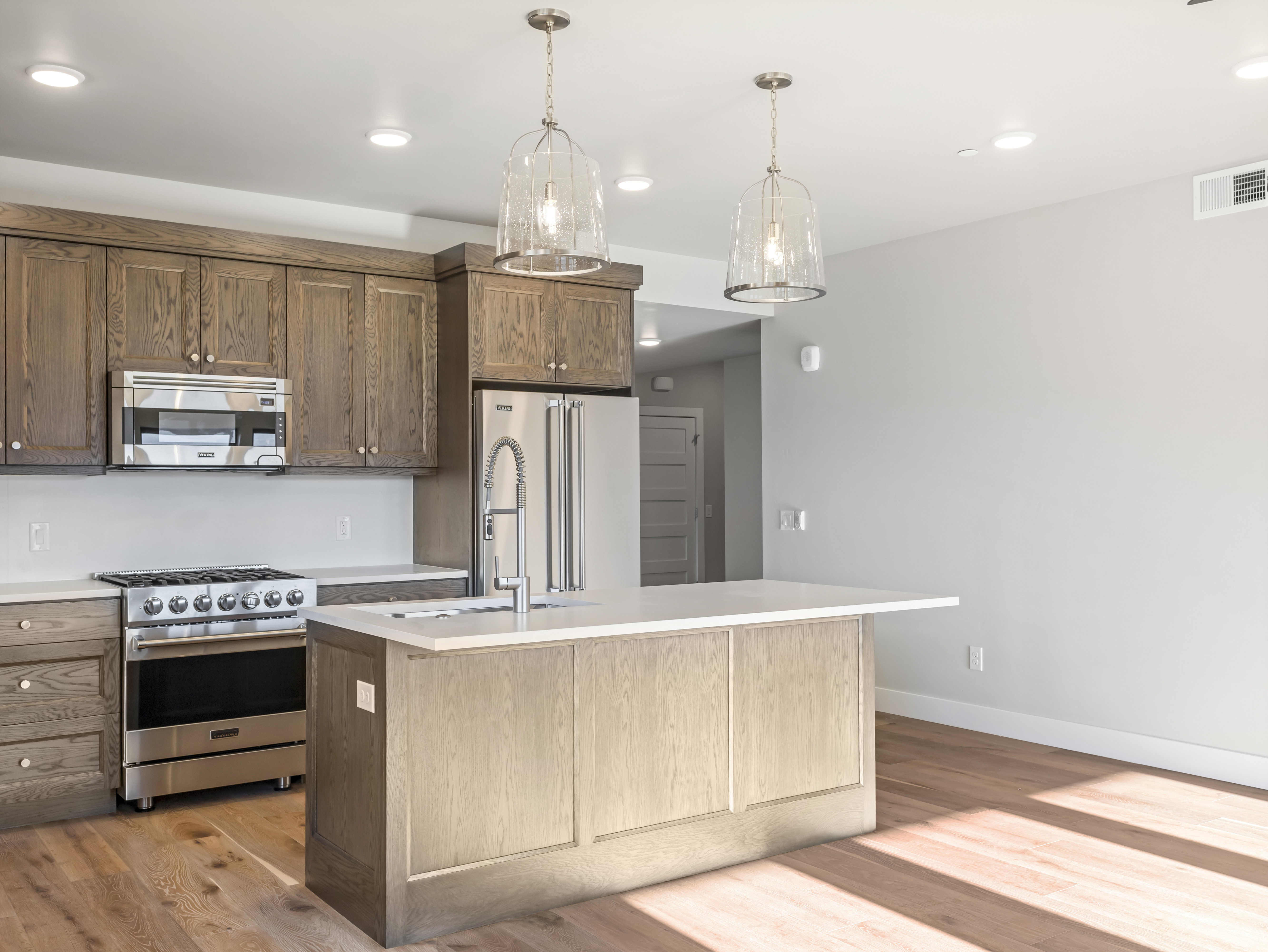 Open-concept kitchen featuring wood-finish cabinetry, stainless steel appliances, a center island with sink, and pendant lighting