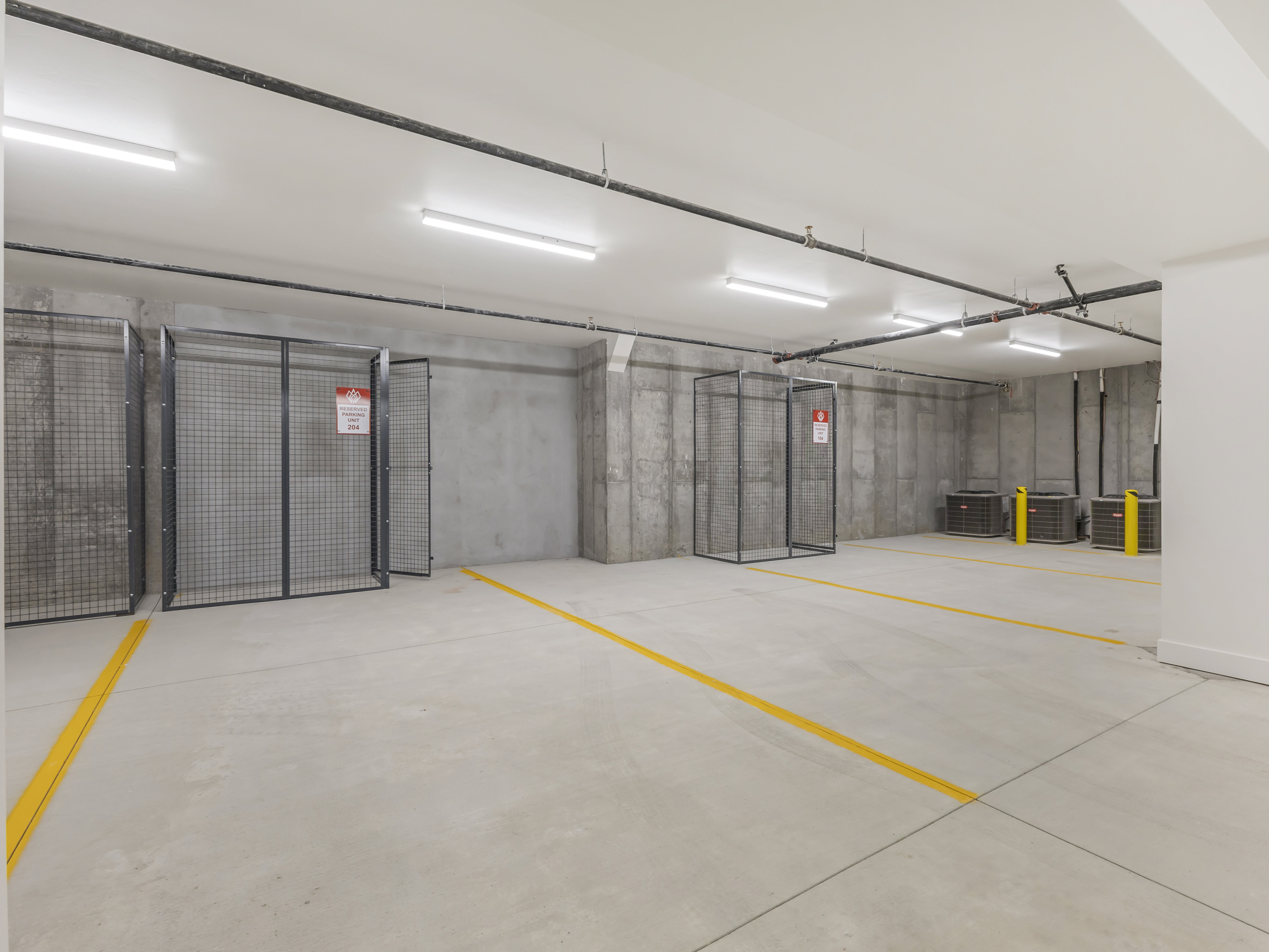 Concrete flooring with yellow demarcation lines, featuring exposed concrete walls and overhead piping