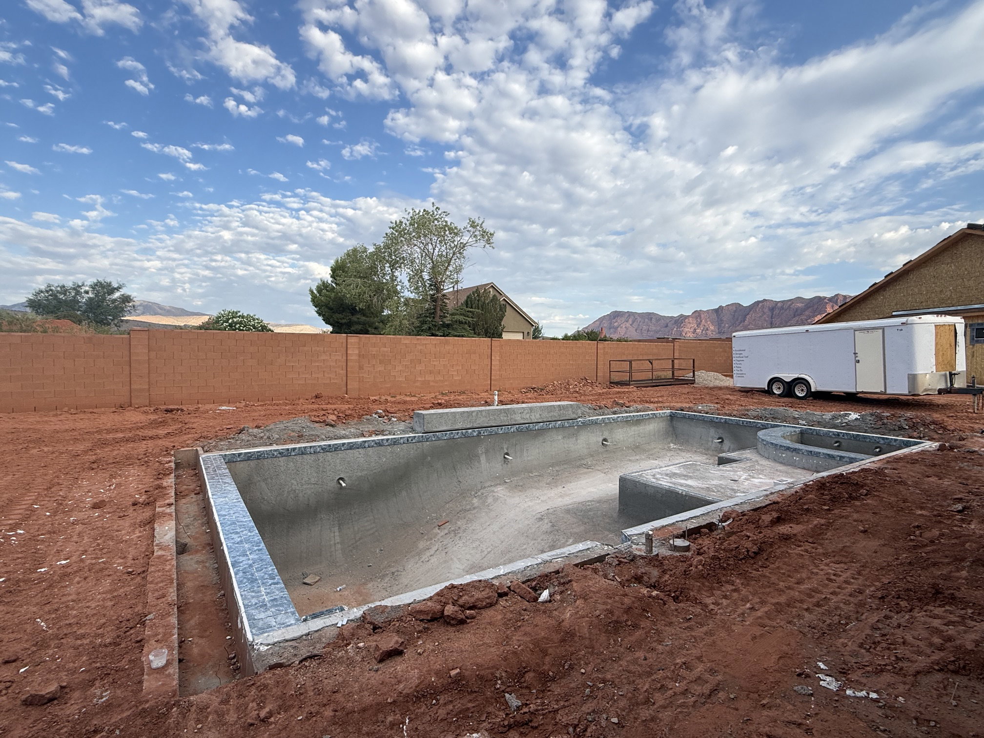 Backyard area featuring an in-ground pool under construction with visible tile work, a surrounding block wall, and distant red rock mountains