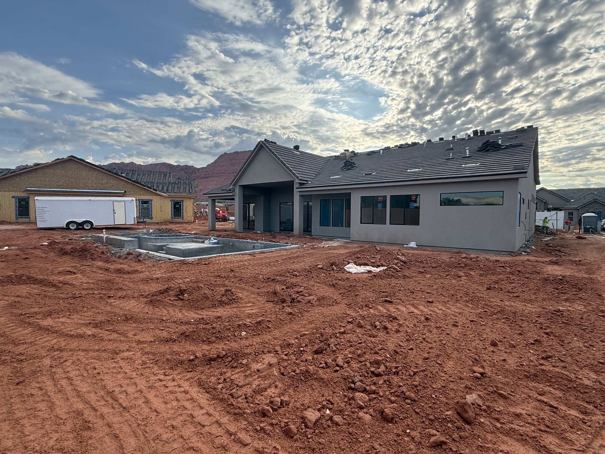 Rear exterior of a single-story residence under construction, featuring a covered patio, multiple windows, and a partially installed shingle roof