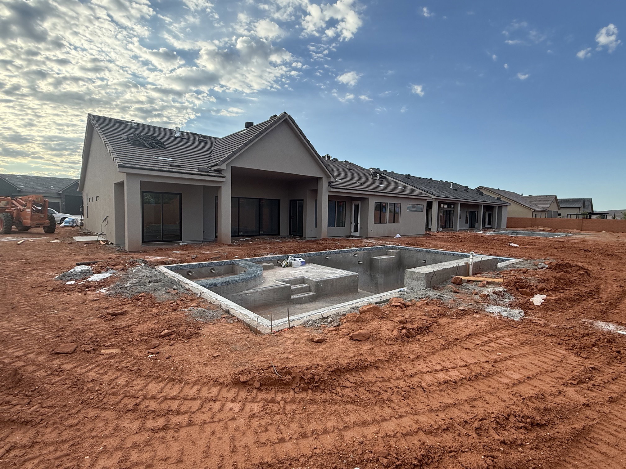 Rear exterior featuring a partially constructed in-ground pool with integrated spa, multiple sliding glass doors, covered patio space, and a neutral stucco finish